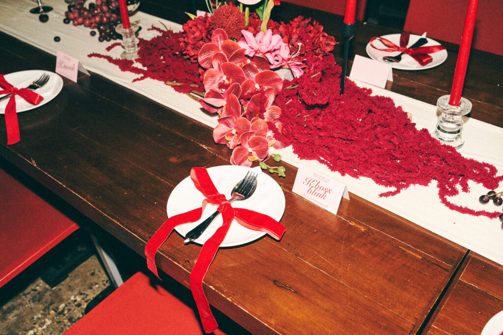 Close-up of a decorated place setting at TUBA Bangkok - a red ribbon tied on the plate, a printed name card and orchids along the table runner