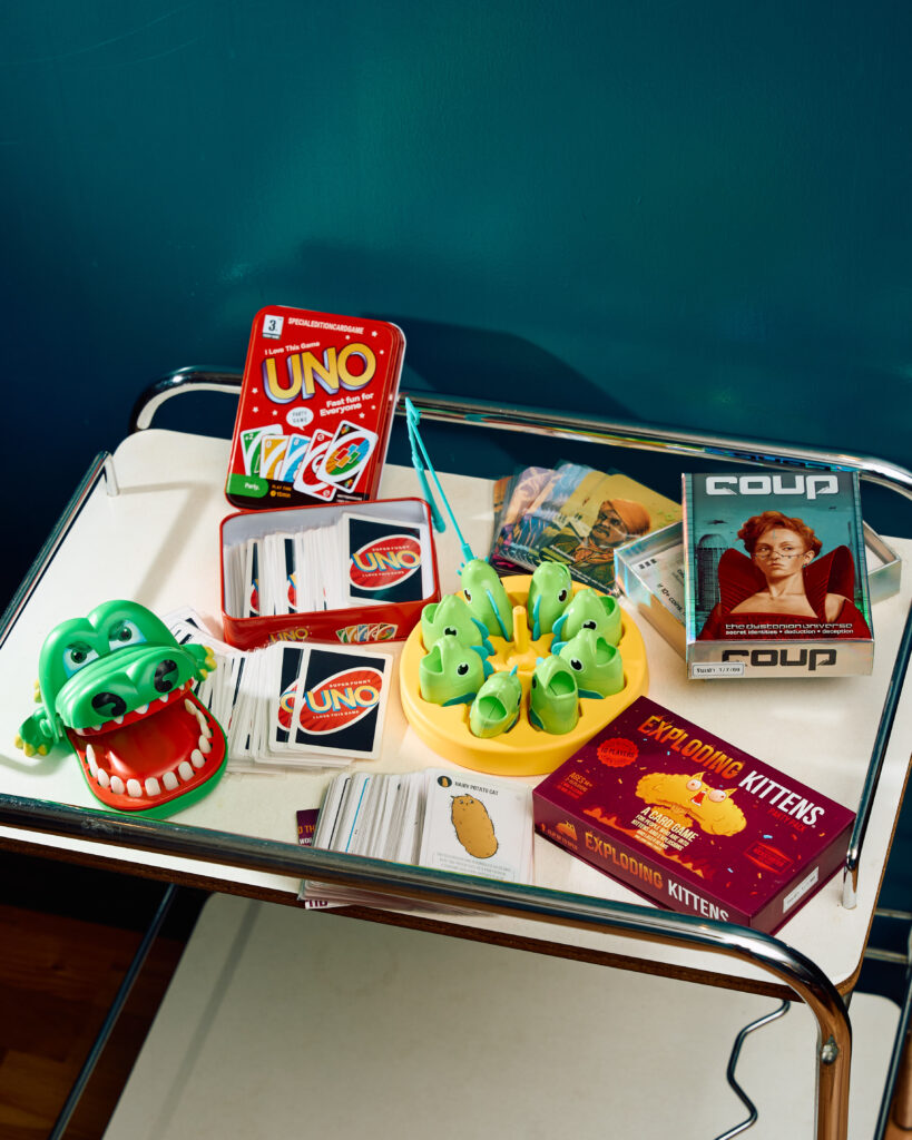 Board games at TUBA Bangkok laid out on a vintage chrome trolley - UNO, Coup, Exploding Kittens, a crocodile game and a fishing game