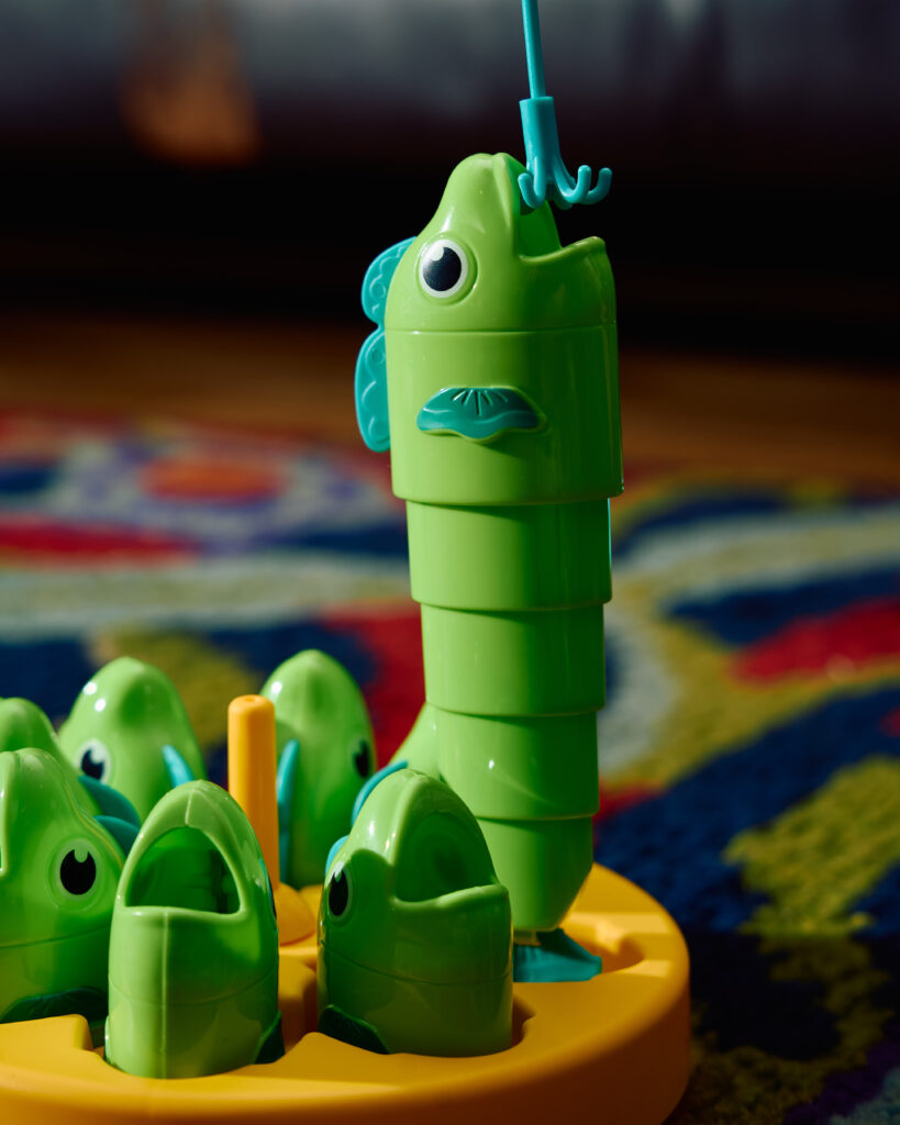 Close-up of the green plastic fishing game on its yellow base, a Thai 1990s childhood toy, on TUBA’s vintage carpet