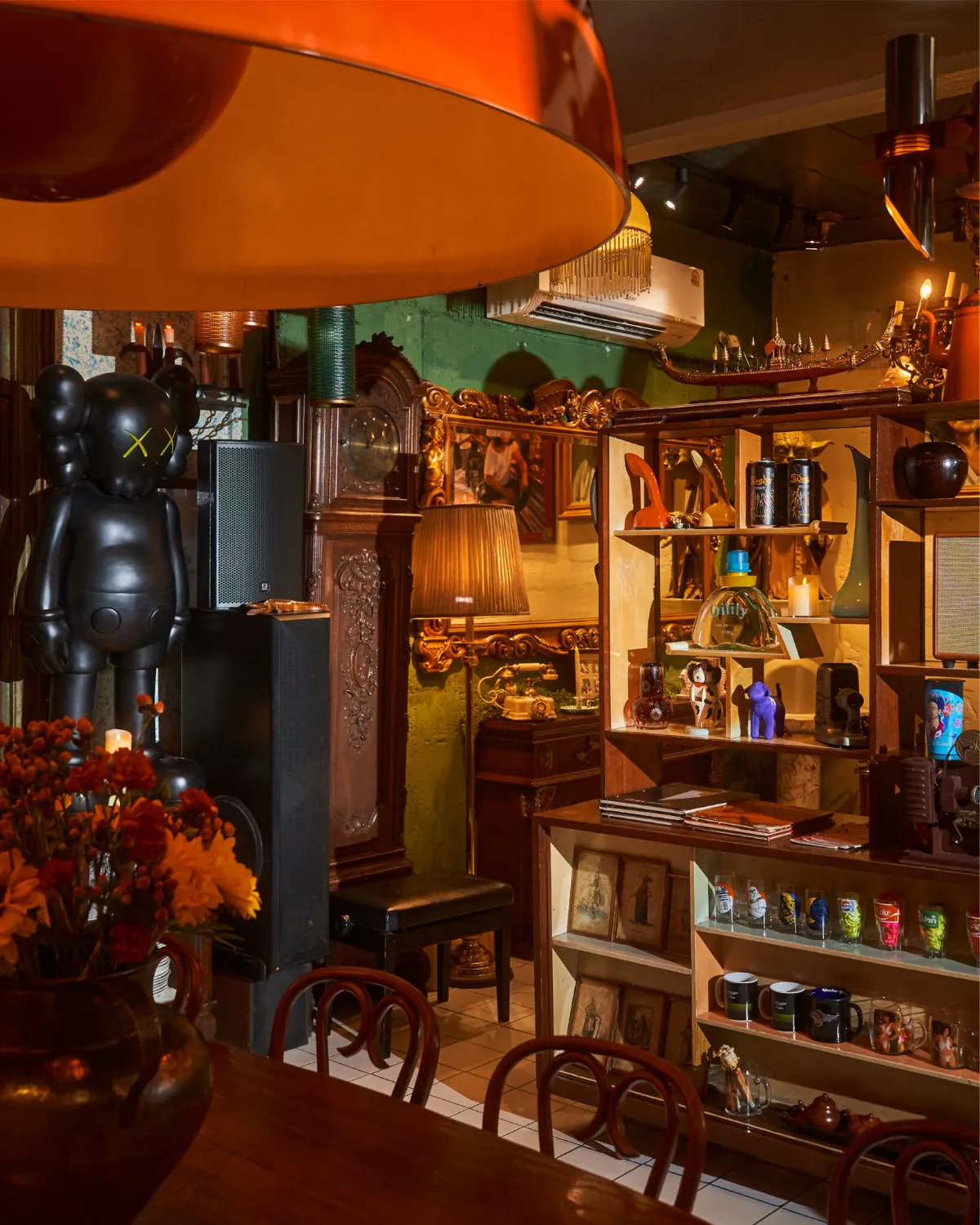 Antique gallery corner at TUBA Bangkok with a large black designer art toy, a grandfather clock and shelves of collectibles