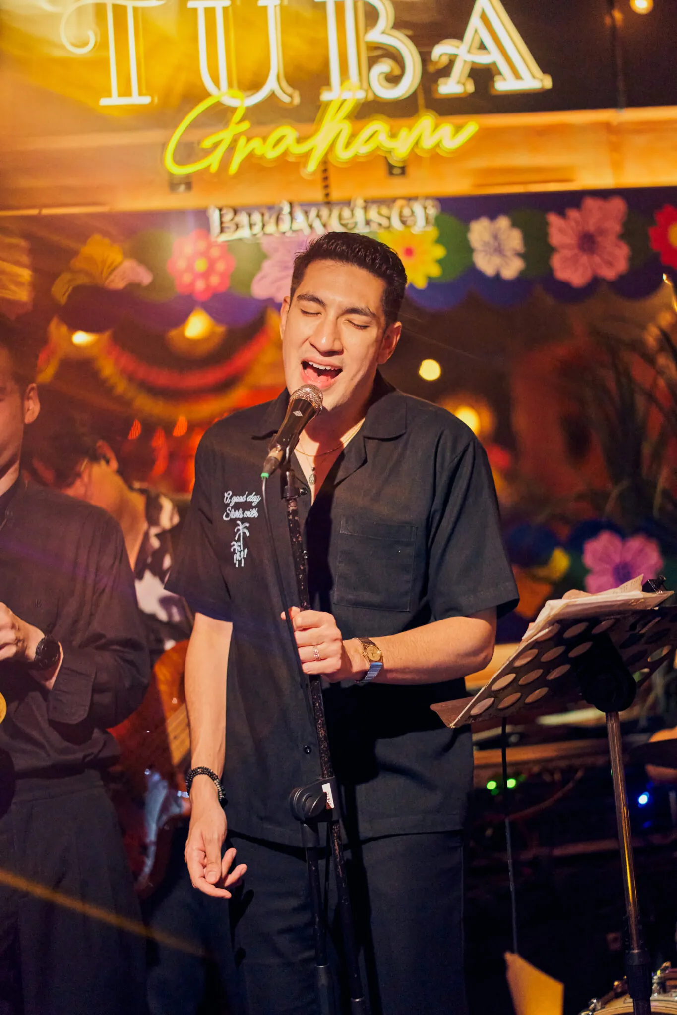 Male vocalist performing live at TUBA Bangkok against a floral vintage backdrop