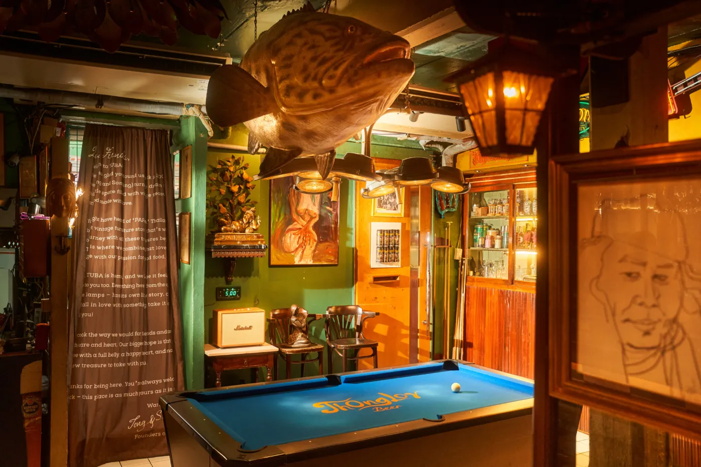 Vintage pool table under warm lamps in the green-walled games room at TUBA Bangkok