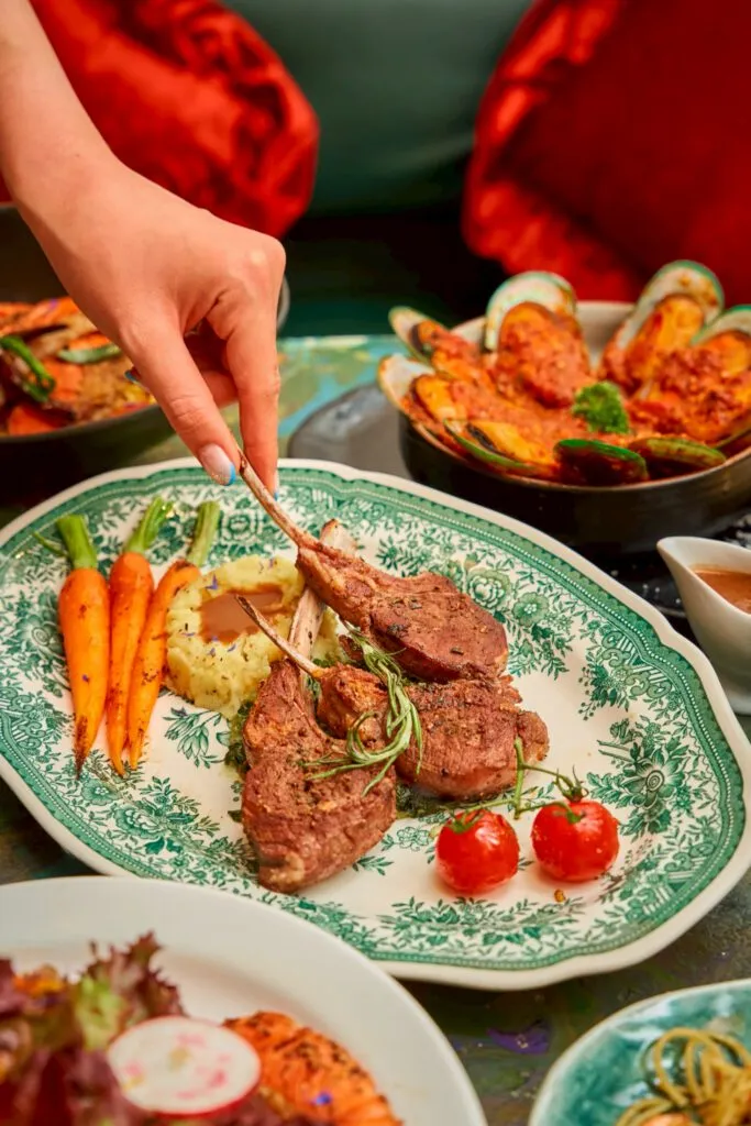 Grilled rack of lamb with mashed potato and baby carrots on an antique green plate at TUBA Bangkok