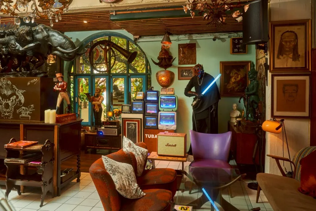 Mint-green lounge at TUBA Bangkok with vintage arcade machines, film figurines and a leather armchair